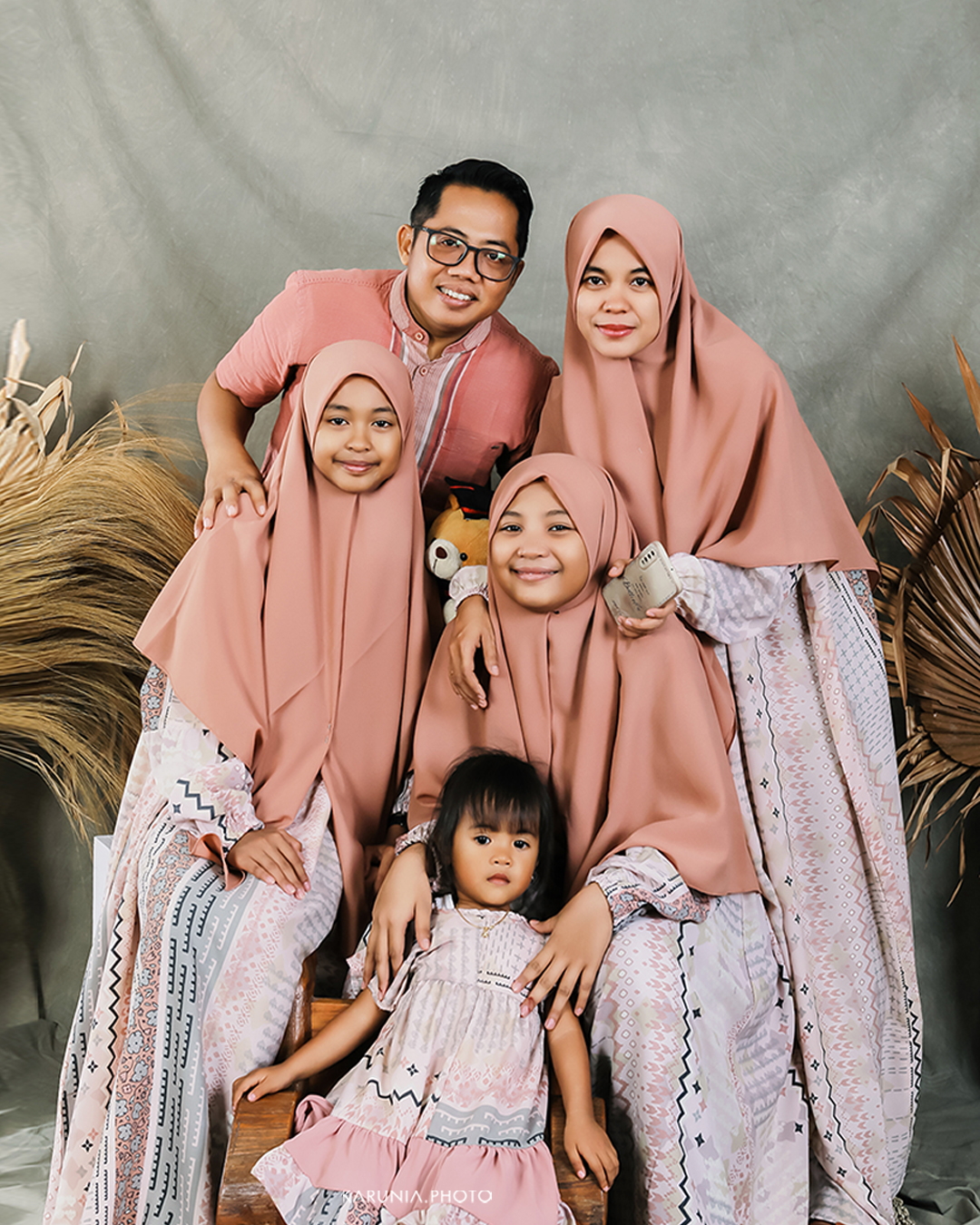 Three siblings sitting on wooden steps in coordinating outfits with genuine smiles and relaxed poses