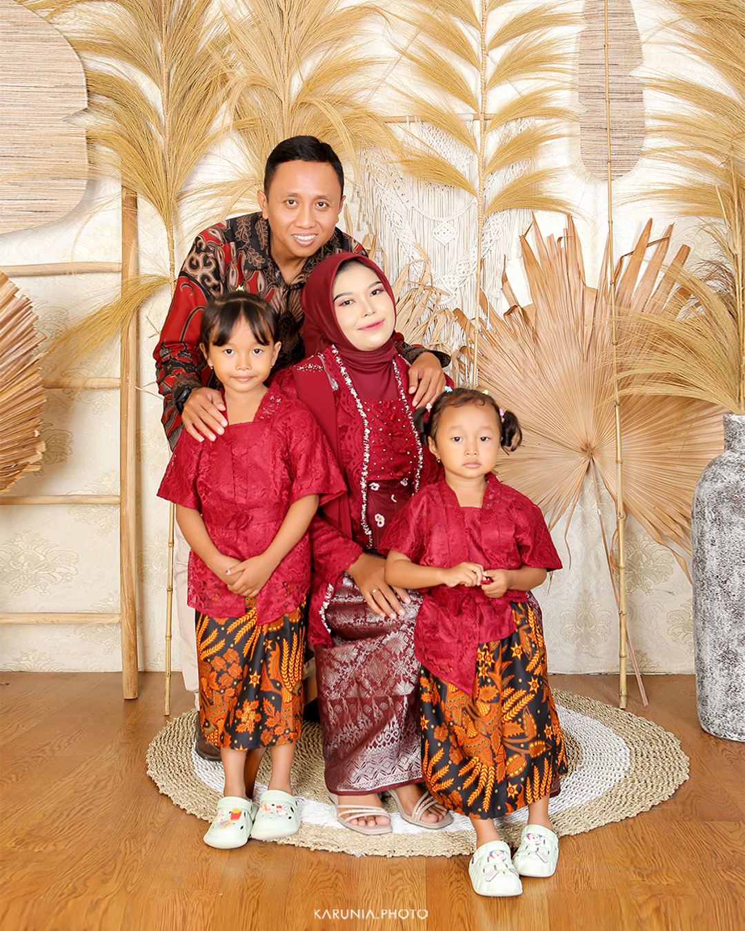 Three siblings sitting on wooden steps in coordinating outfits with genuine smiles and relaxed poses