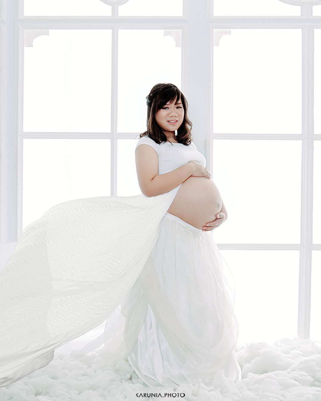 Couple embracing with father-to-be kissing mother's belly in soft studio lighting