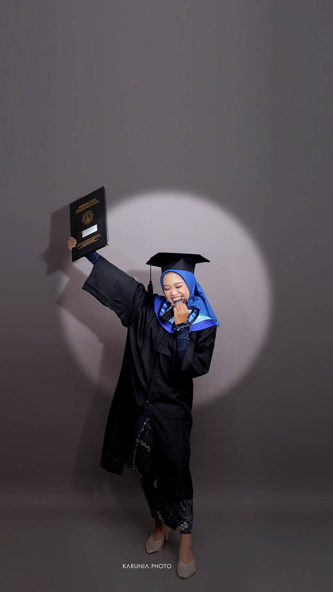 Graduation portrait showing a young woman in cap and gown holding diploma with proud expression